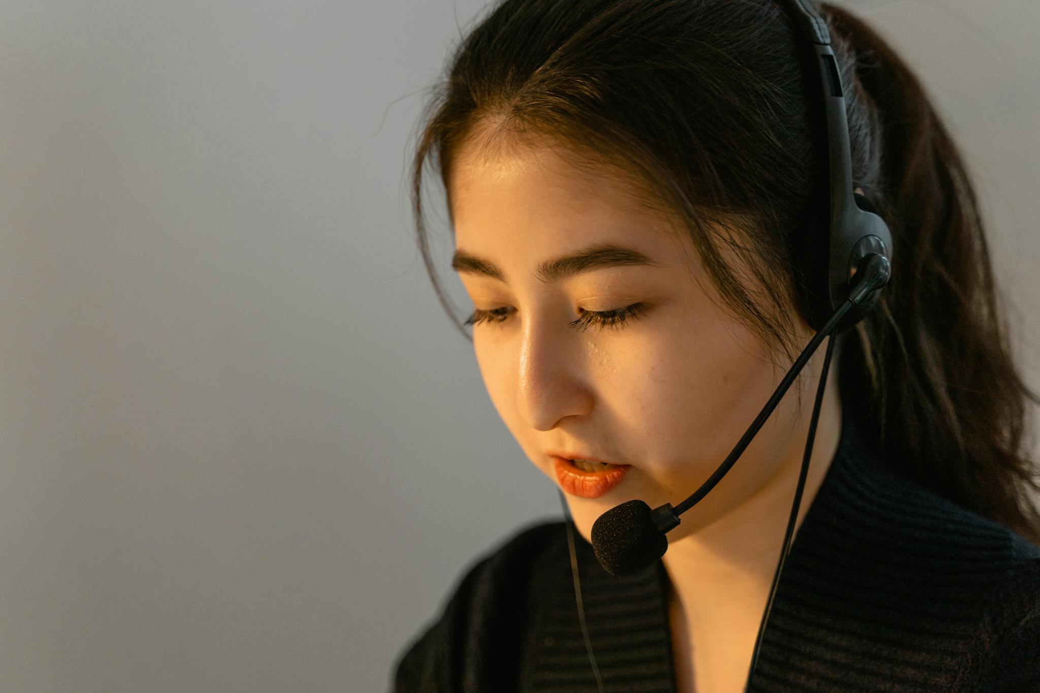 Focused young woman in headset working in customer support, speaking attentively.